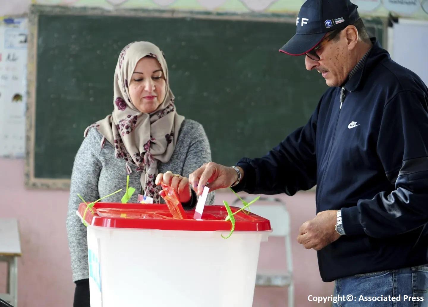 Person in Tunisia putting ballot in box while another observes. 