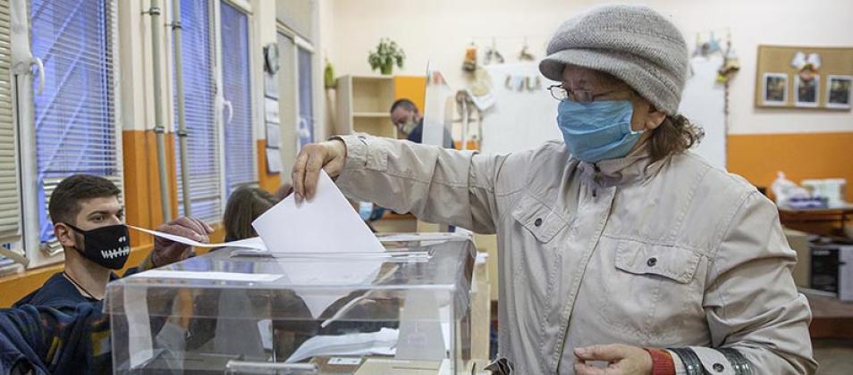 A person wearing a mask puts a ballot into a ballot box.