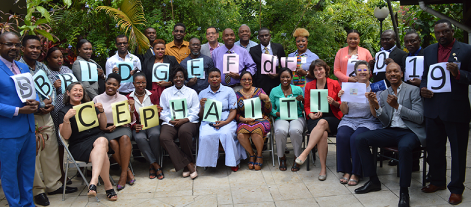 Participants and facilitators from the TtF workshop hold up signs that spell out, "BRIDGE FdF 2019 CEP Haiti USAID" 