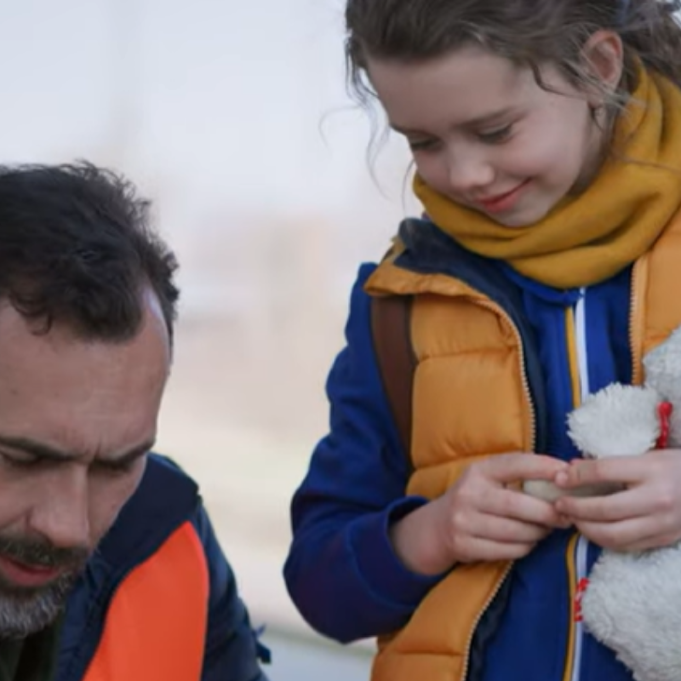 Screenshot from about IFES Ukraine video. Man holding clipboard with young girl holding stuffed animal. 