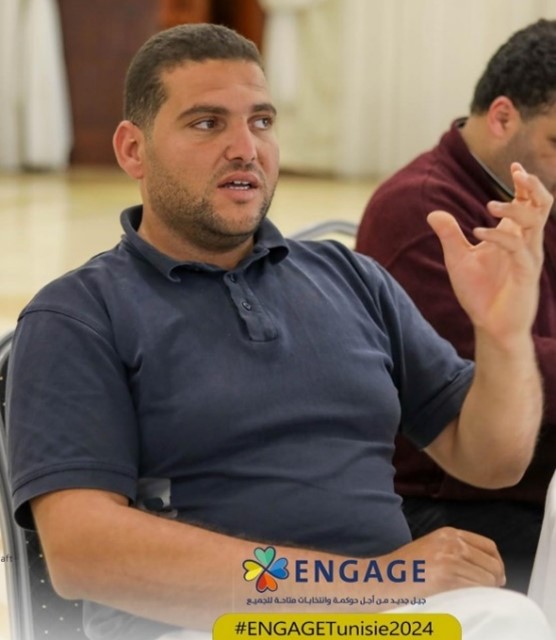 Nabil in a classroom with one arm raised