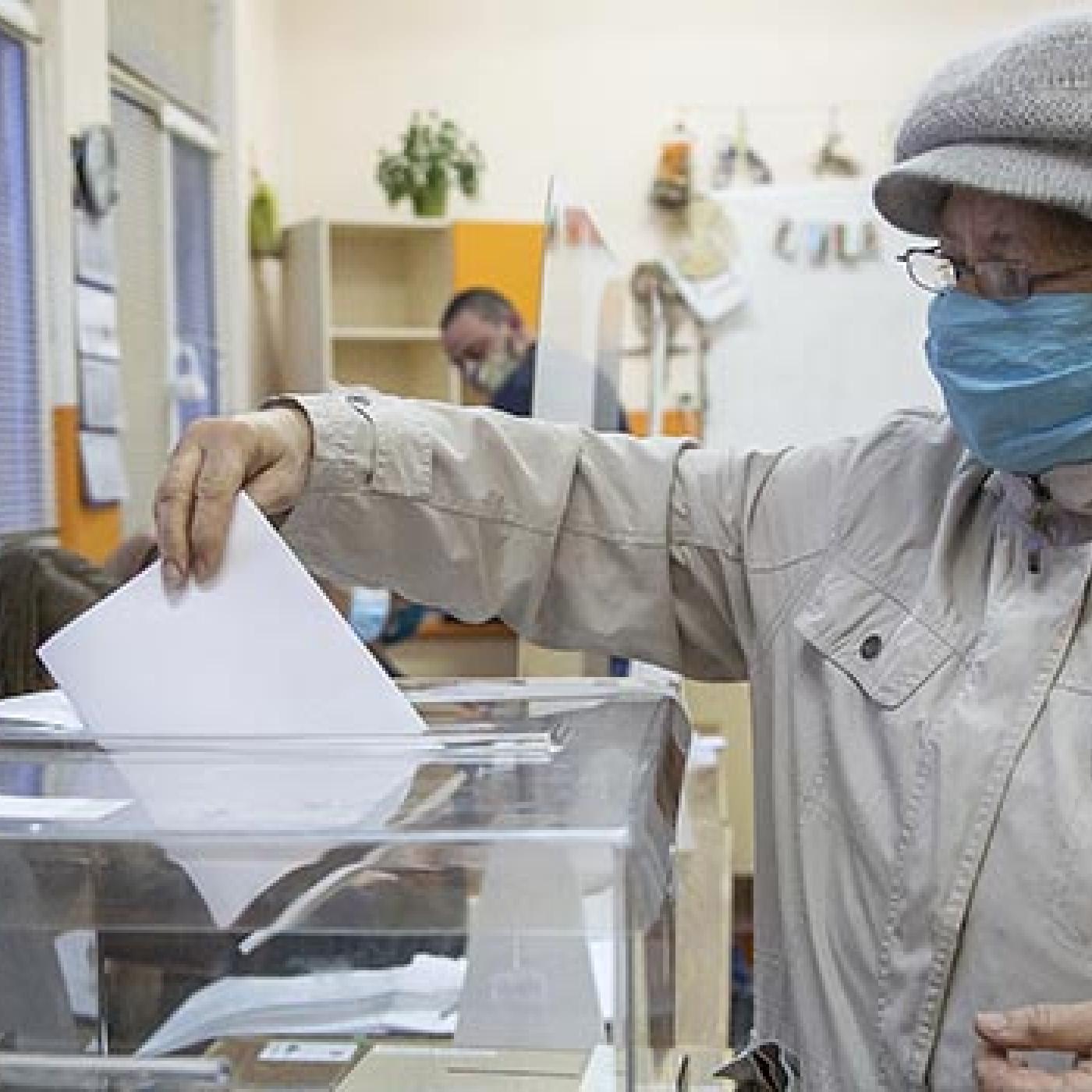 A person wearing a mask puts a ballot into a ballot box.